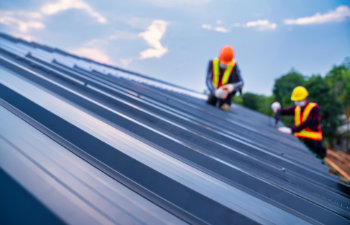 roofer worker safety wear using pneumatic nail gun and installing on new roof metal sheet