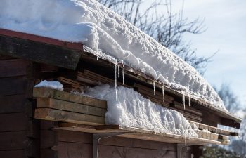 Snow-covered wooden roof with icicles hanging from the edge, set against a clear sky.