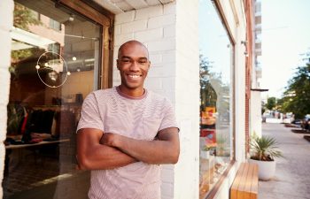 Young black man smiling to camera outside his clothes shop