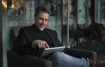 Businessman using tablet computer in office. Happy middle aged man in business casual, Entrepreneur working online, reading finance report, thinking.